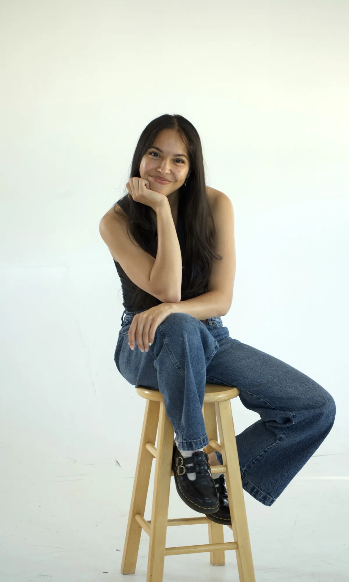 Nyss Alvarado, founder of Savado Sites, sitting on a wooden stool